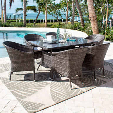 Outdoor dining set with table and chairs on a patio by a pool with palm trees and ocean view.