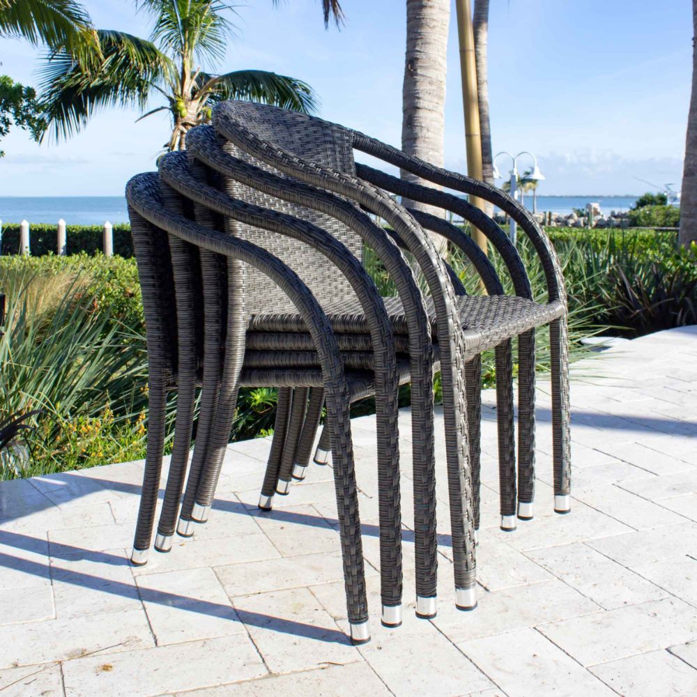 Stack of wicker chairs on a patio with palm trees and ocean view