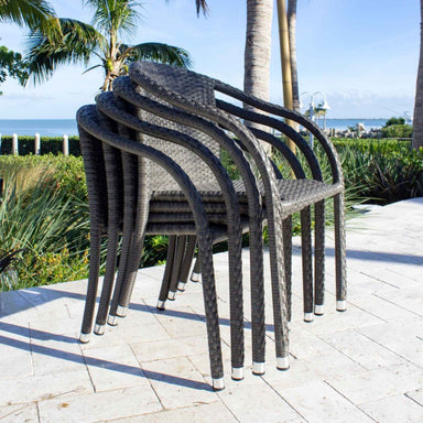 Stack of wicker chairs on a patio with palm trees and ocean view