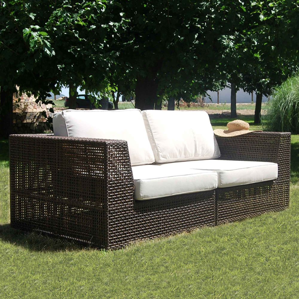 Outdoor wicker sofa with white cushions on a grassy area with trees in the background