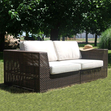 Outdoor wicker sofa with white cushions on a grassy area with trees in the background