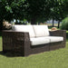Outdoor wicker sofa with white cushions on a grassy area with trees in the background