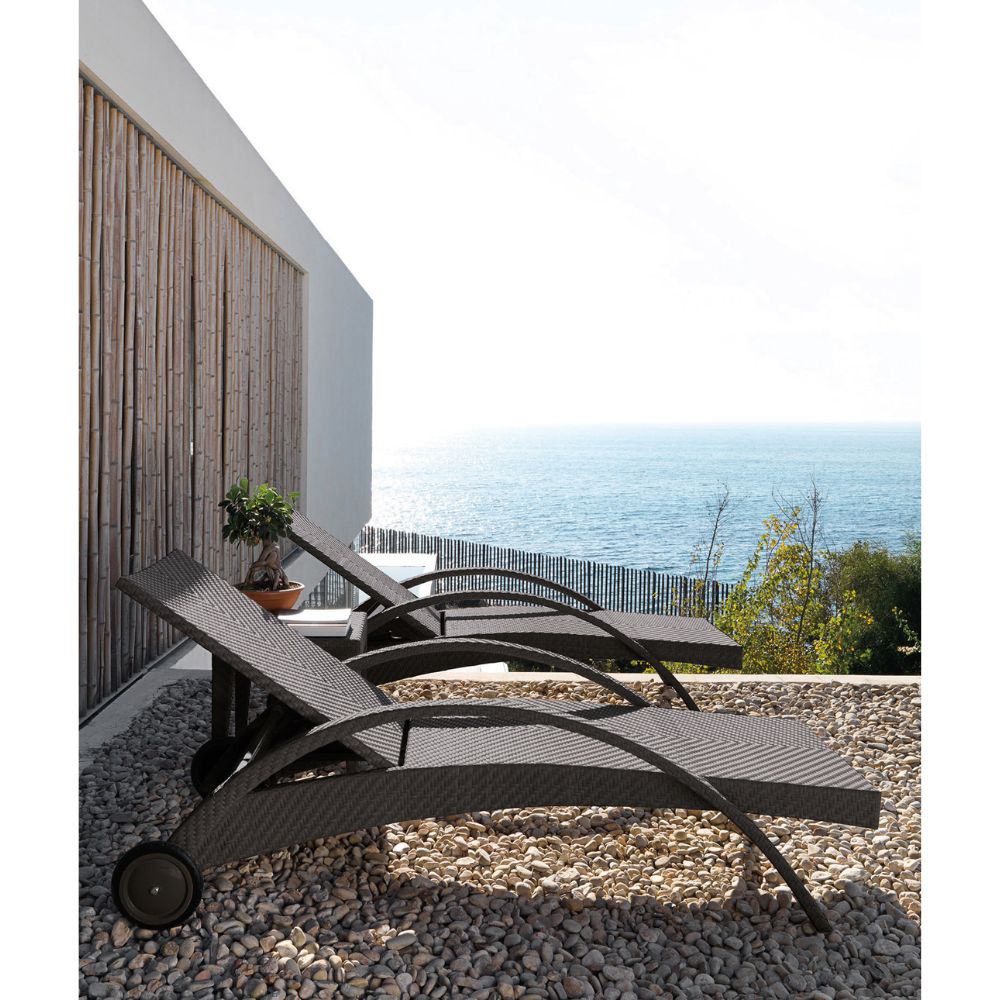 Two black lounge chairs on a pebble surface with a scenic ocean view in the background.