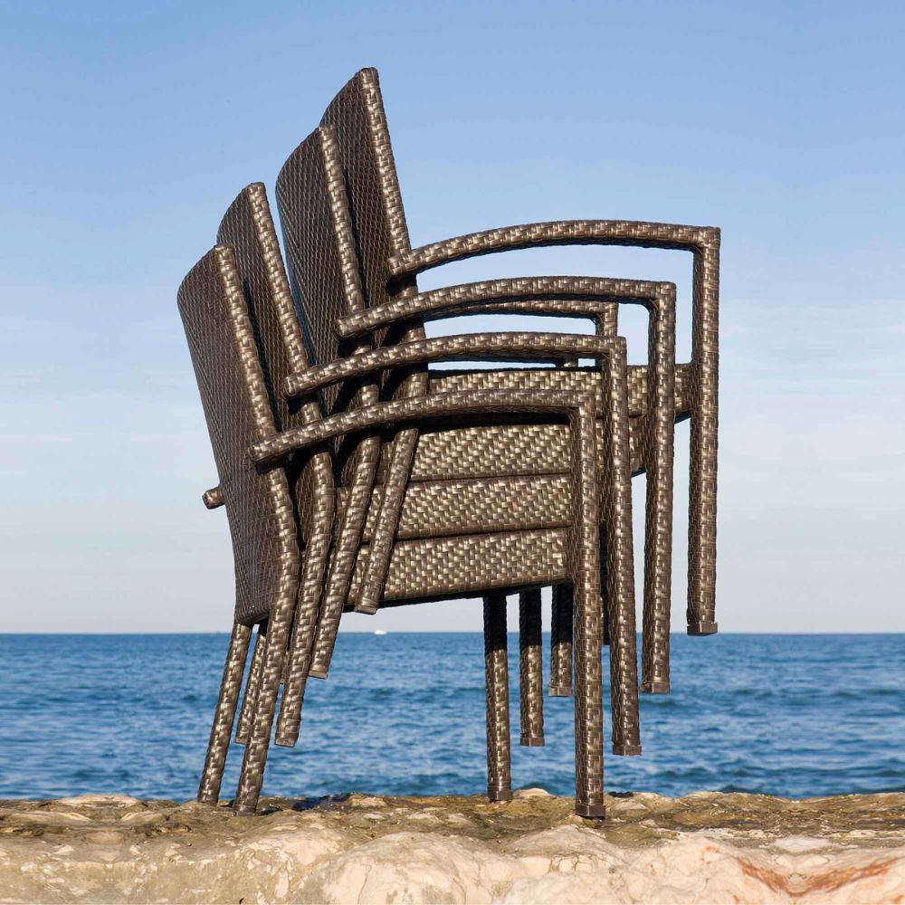 Stack of woven chairs on a rocky surface with ocean and clear sky in the background