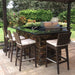 Outdoor kitchen with grill, bar stools, and a stone countertop in a garden setting.