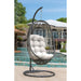 Hanging egg-shaped chair with white cushion in front of a pool and house.
