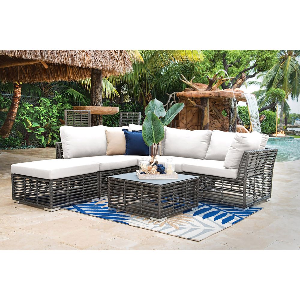 Outdoor patio furniture set with cushions on a patio with a pool and tropical plants in the background.
