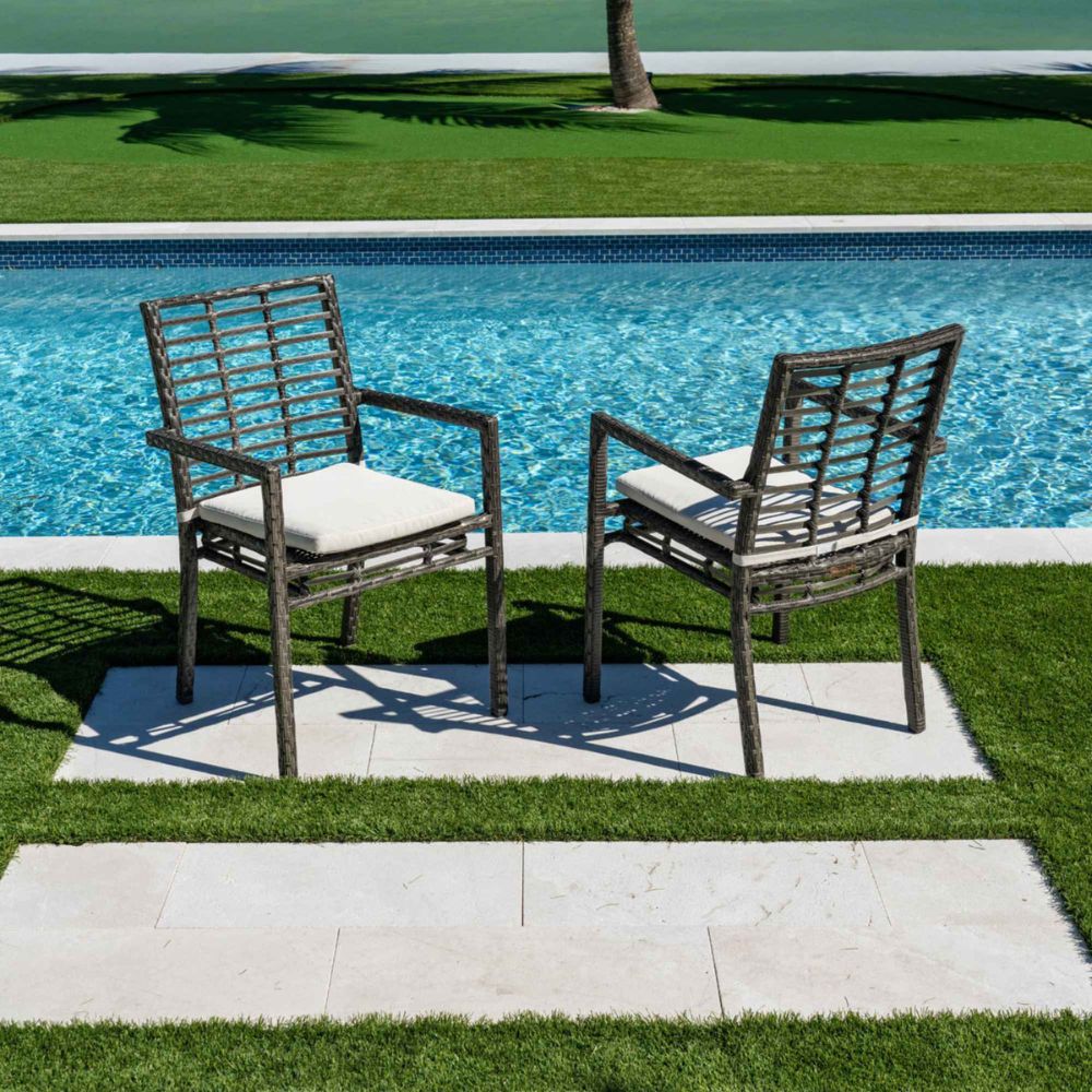 Two wicker chairs with white cushions by a poolside on a sunny day.