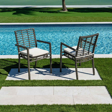Two wicker chairs with white cushions by a poolside on a sunny day.