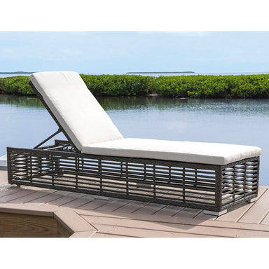 Wicker sun lounger with white cushion on a wooden deck by a pool