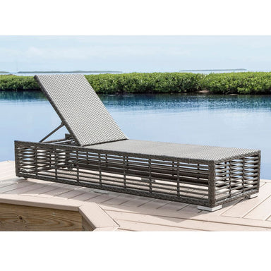 Wicker sun lounger on a wooden deck by a pool with greenery in the background