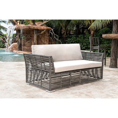 Outdoor wicker sofa with beige cushions in a tropical setting with a water feature.