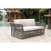Outdoor wicker sofa with beige cushions in a tropical setting with a water feature.