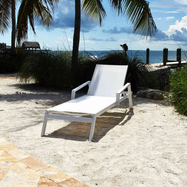 White lounge chair on a sandy beach with palm trees and ocean in the background