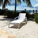 White lounge chair on a sandy beach with palm trees and ocean in the background