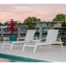 Two white lounge chairs by a pool with a sunset sky and building in the background.
