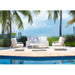 Outdoor patio set with white furniture by a pool, palm trees in the background