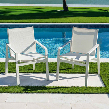 Two white chairs on a patio by a pool with grass and water in the background
