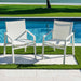 Two white chairs on a patio by a pool with grass and water in the background