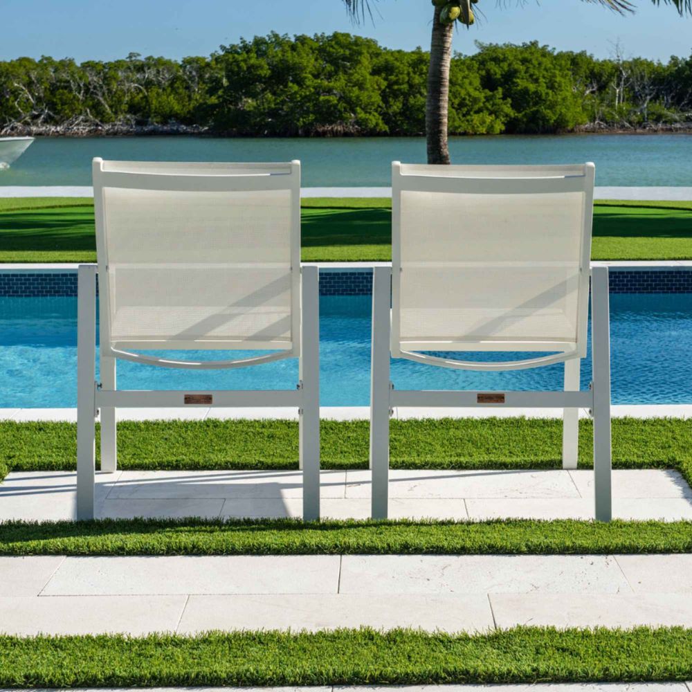 Two white chairs by a pool with a scenic background of water and trees.