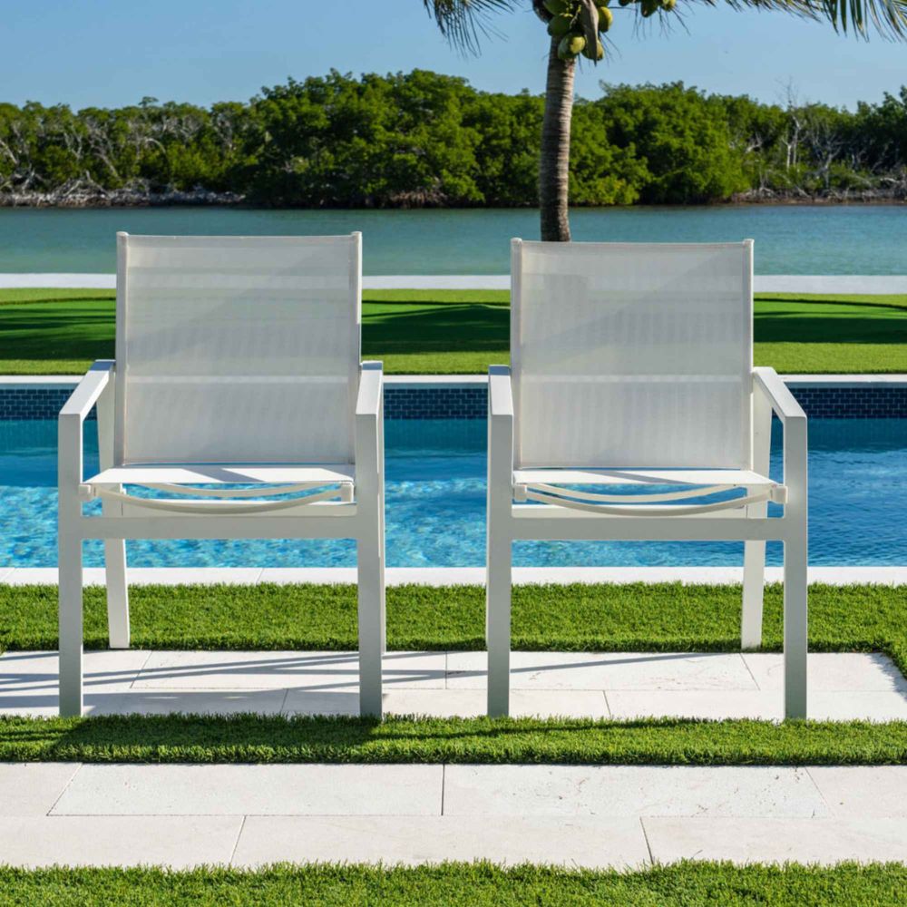 Two white chairs on a patio by a pool with a scenic background