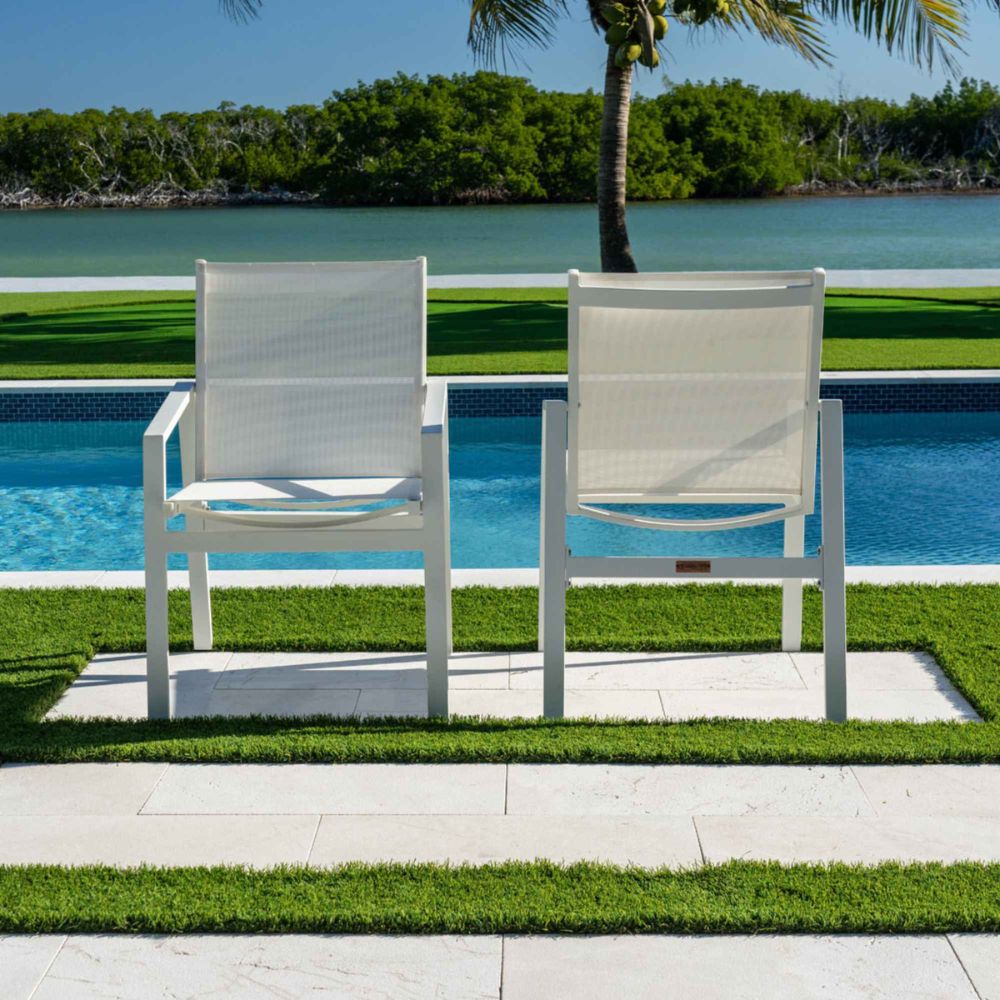 Two white chairs on a patio overlooking a pool and greenery.
