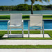 Two white chairs on a patio overlooking a pool and greenery.