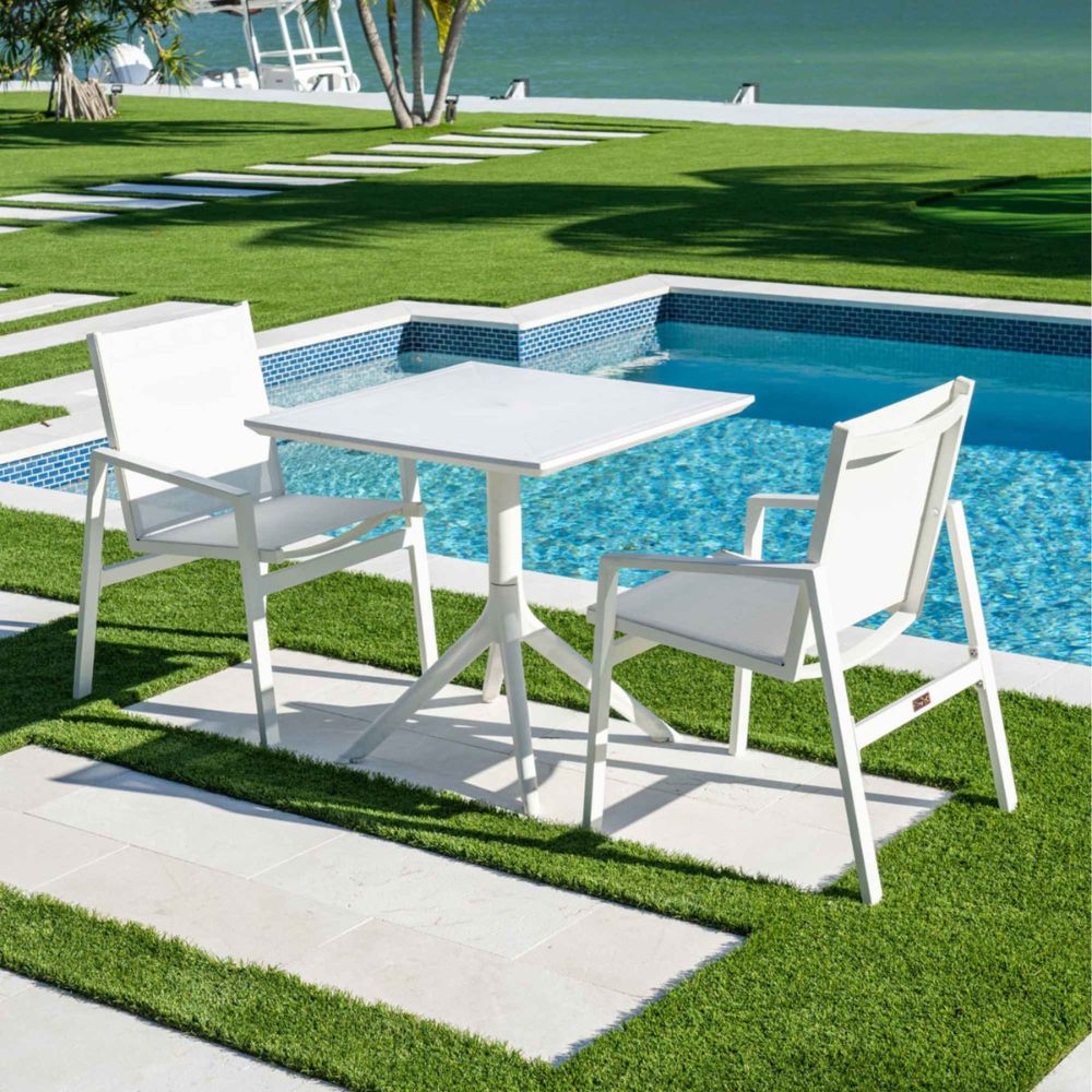 White outdoor table and chairs by a poolside with green grass and water in the background