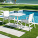 White outdoor table and chairs by a poolside with green grass and water in the background