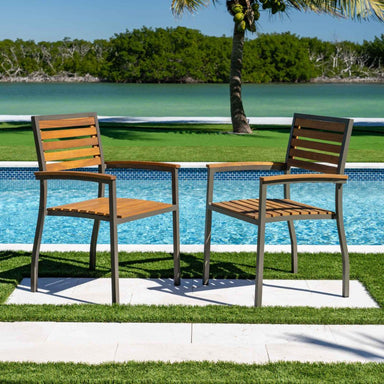 Two wooden chairs with metal frames by a poolside with greenery in the background