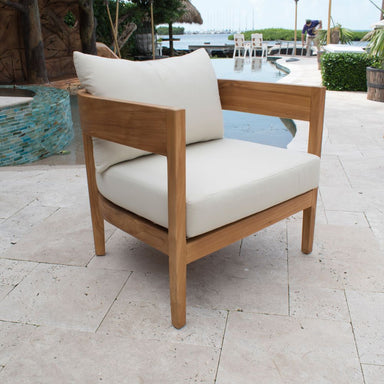 Wooden chair with white cushions on a patio area near a pool.