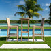 Outdoor patio set with a table and chairs by a pool with palm trees in the background.