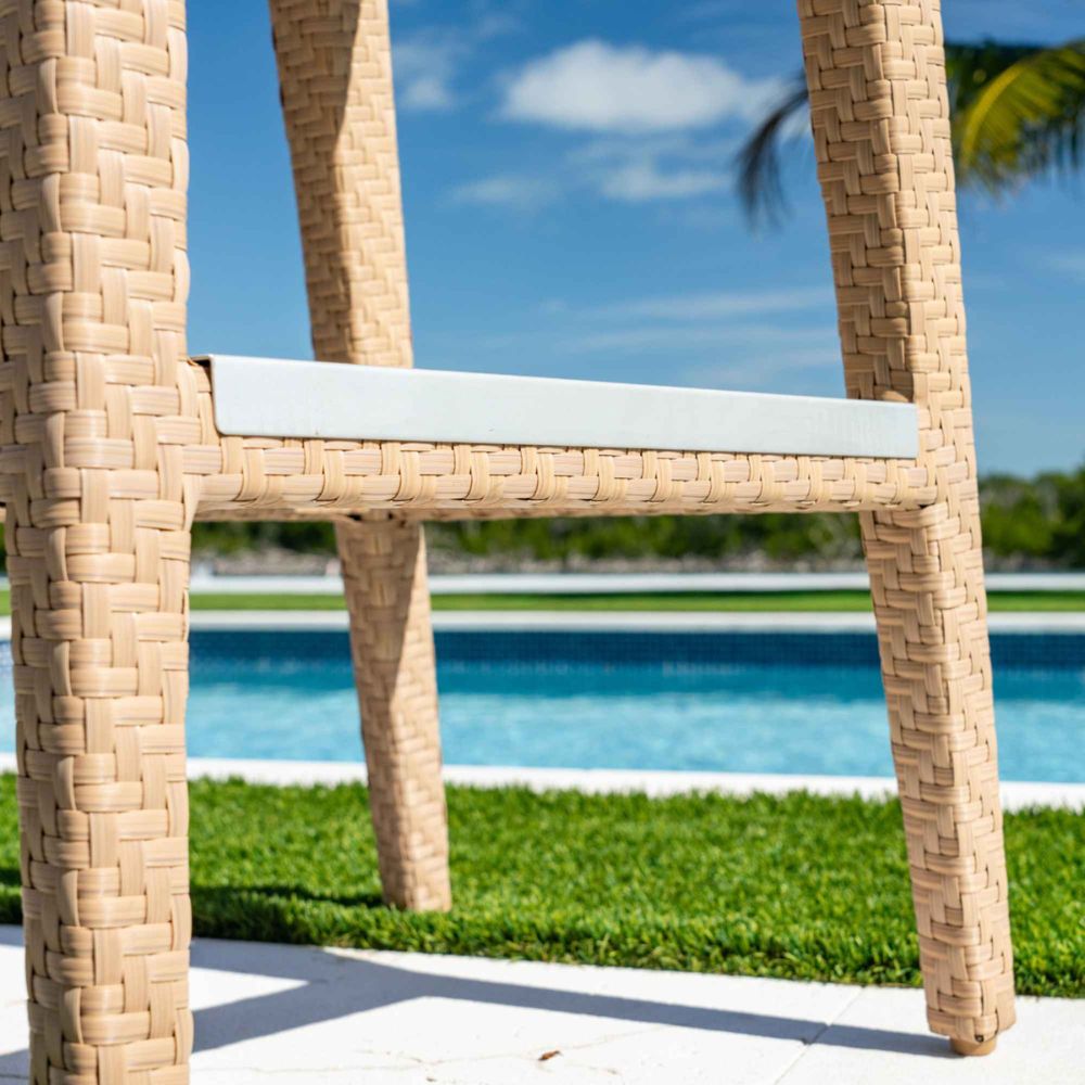 Wicker chair with a blue cushion by a poolside with green grass and blue sky.