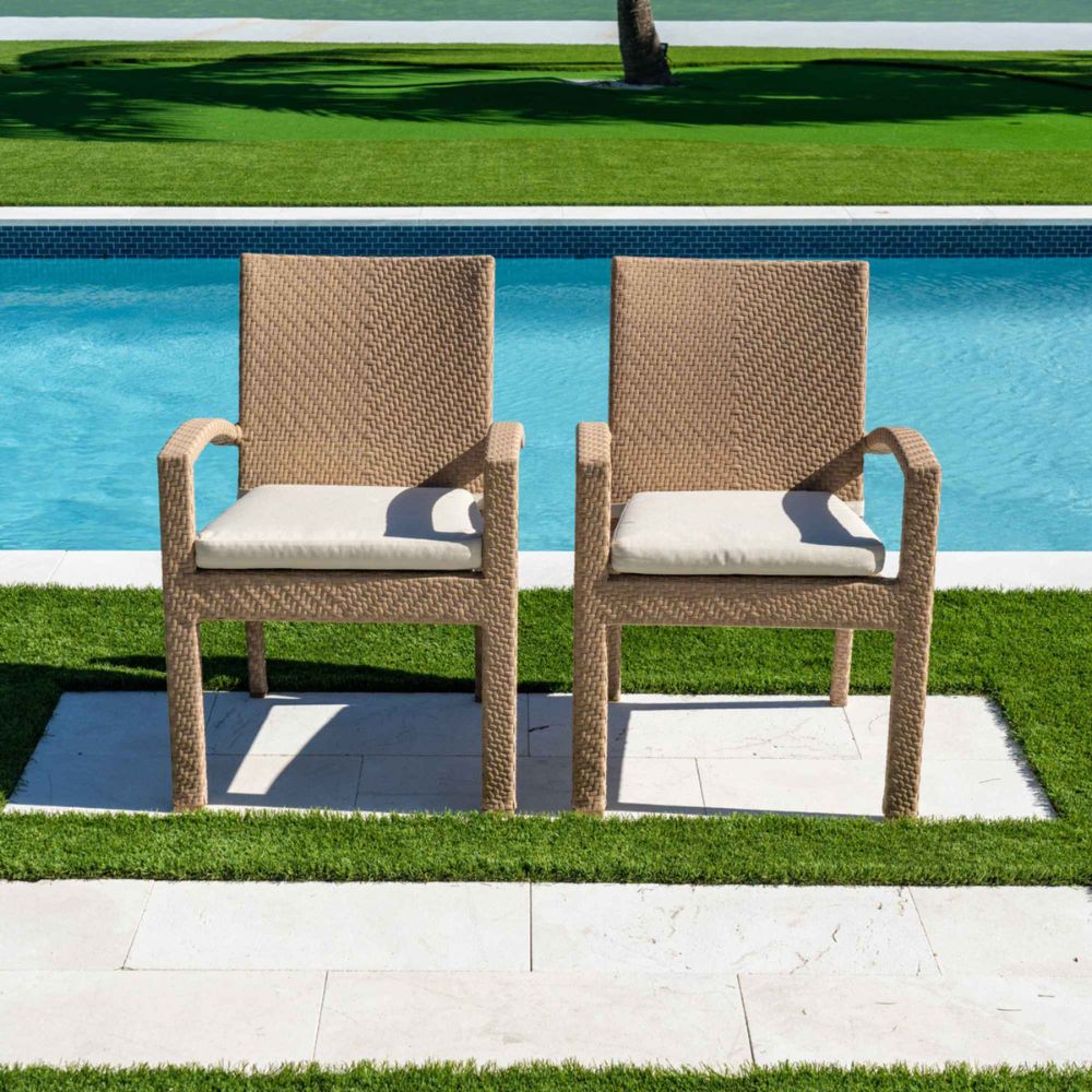 Two wicker chairs with cushions by a poolside on a sunny day.