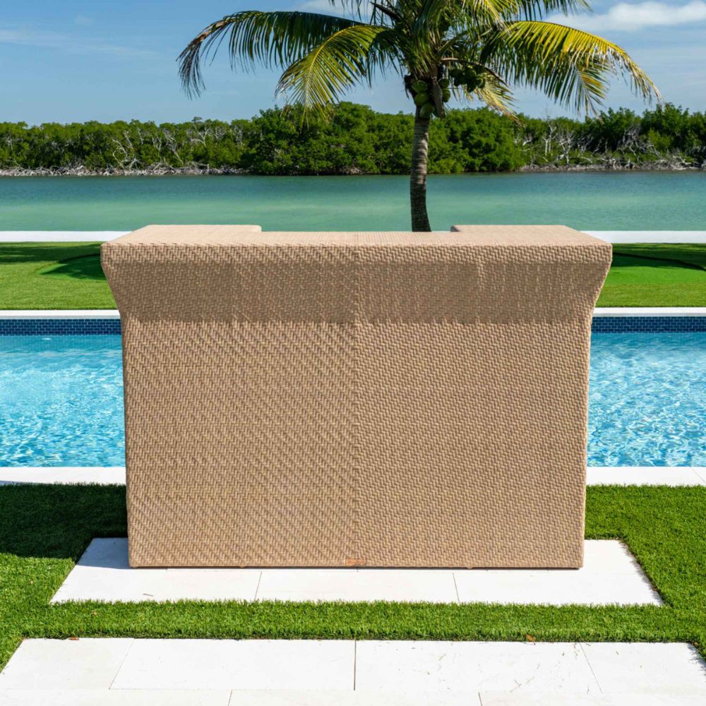 Beige woven outdoor furniture piece by a pool with palm tree and water in the background