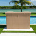 Beige woven outdoor furniture piece by a pool with palm tree and water in the background