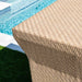 Close-up of a woven outdoor stool with a pool in the background