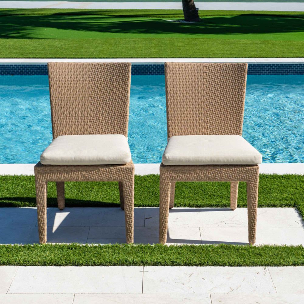 Two wicker chairs with beige cushions by a poolside.