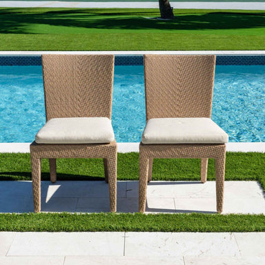 Two wicker chairs with beige cushions by a poolside.