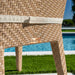 Close-up of woven outdoor furniture with a blurred pool and greenery in the background