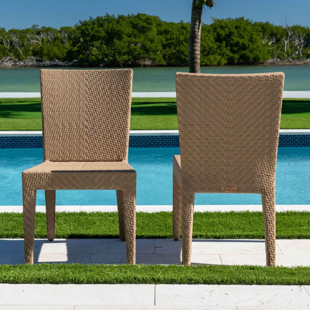 Two wicker chairs by a pool with greenery in the background