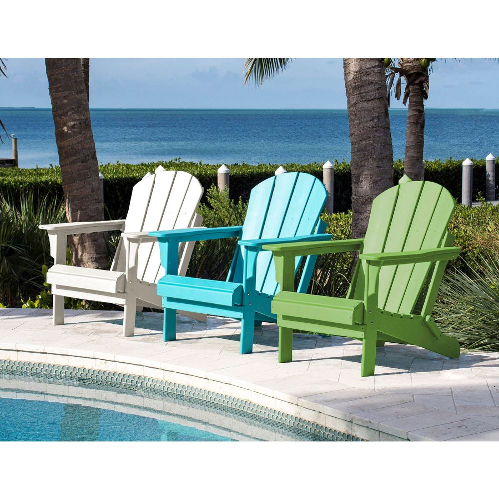 Three Adirondack chairs in white, blue, and green by a pool with ocean view.