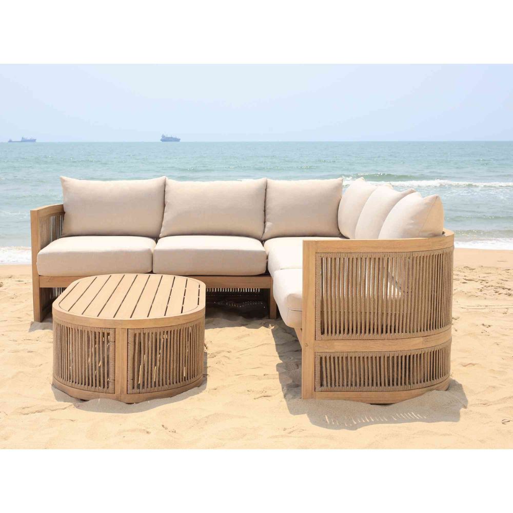 Outdoor furniture set with beige sofa, chair, and table on a sandy beach.