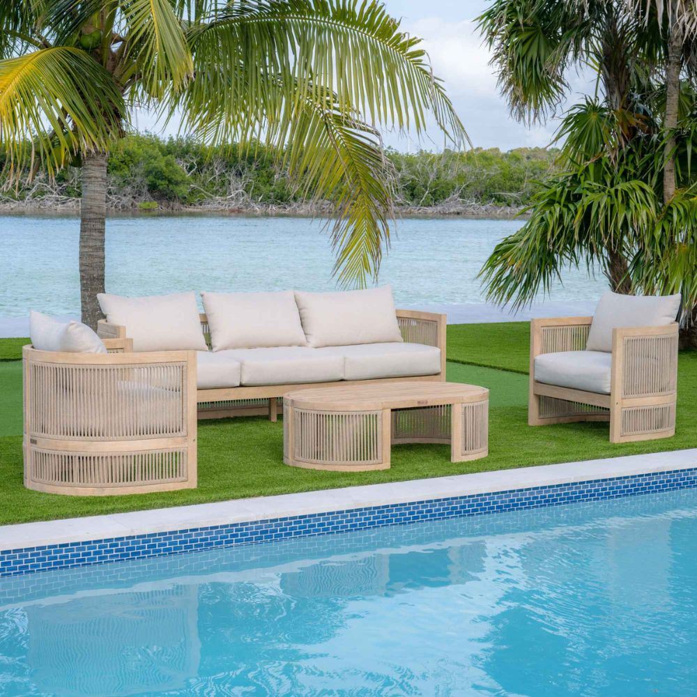 Outdoor furniture set with beige cushions by a poolside with palm trees and water in the background