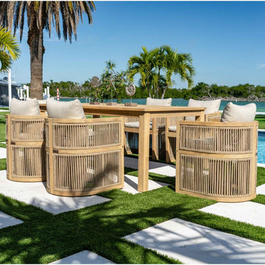 Outdoor furniture set with wooden chairs and table on a grassy area with palm trees and pool in the background.