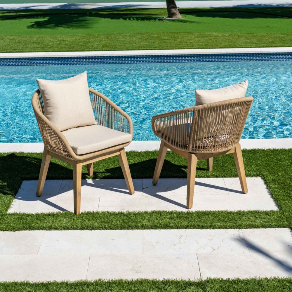 Two wicker chairs with beige cushions by a poolside.