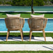Two wicker chairs with cushions by a poolside with greenery in the background