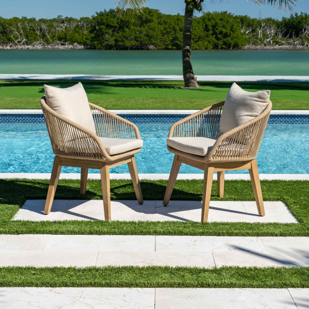 Two wicker chairs with beige cushions by a poolside with greenery in the background