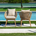 Two wicker chairs with beige cushions by a poolside with greenery in the background