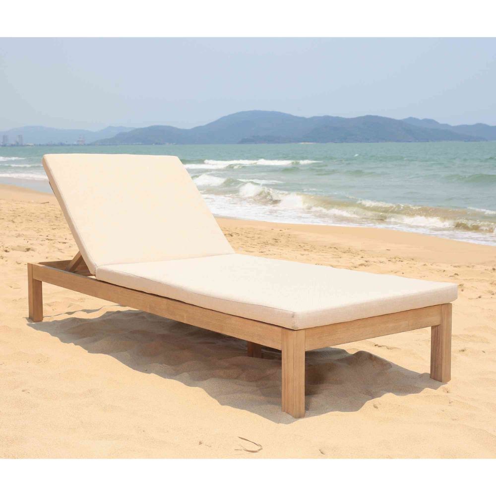 Wooden sun lounger with beige cushion on a sandy beach with ocean and mountains in the background